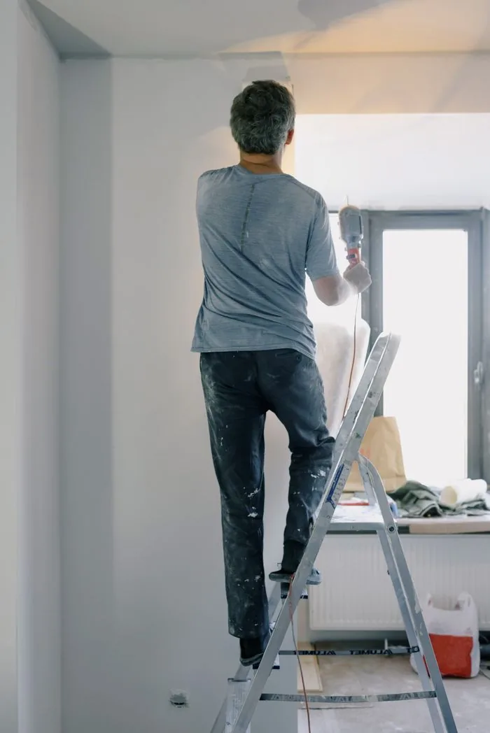 Klusser op een trap werkt met een boormachine aan het plafond van een kamer die wordt verbouwd